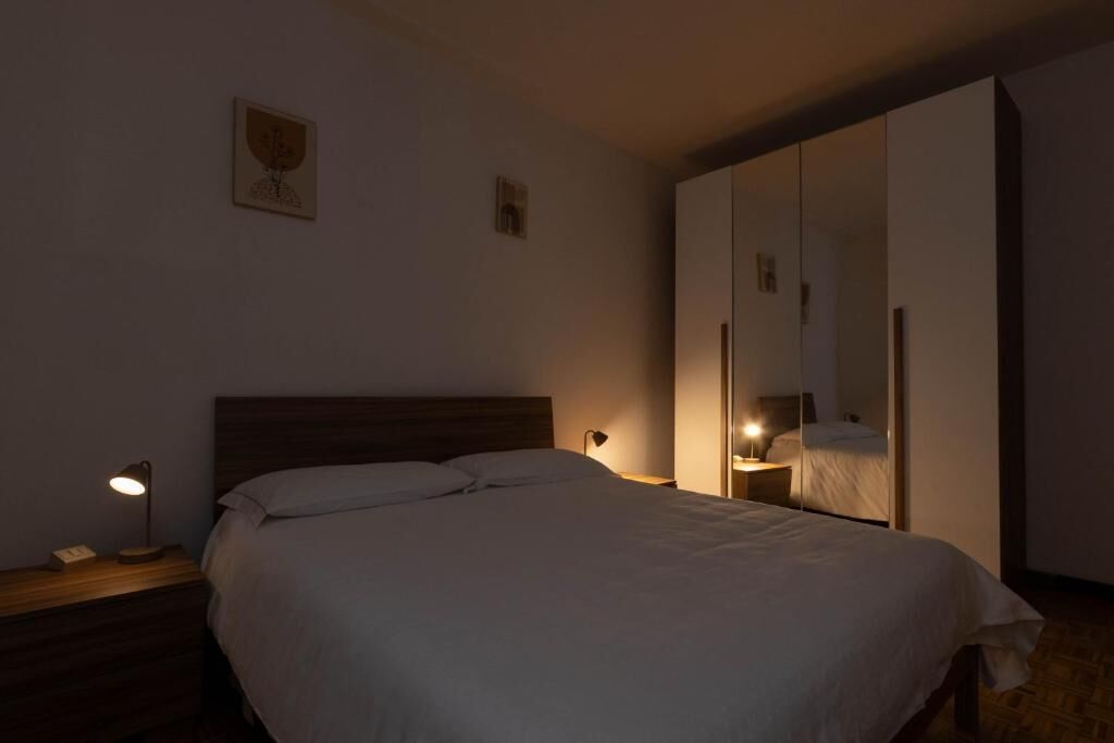 A bedroom with a bed, bedside lamps, a nightstand, a wardrobe, and a wall-mounted mirror.