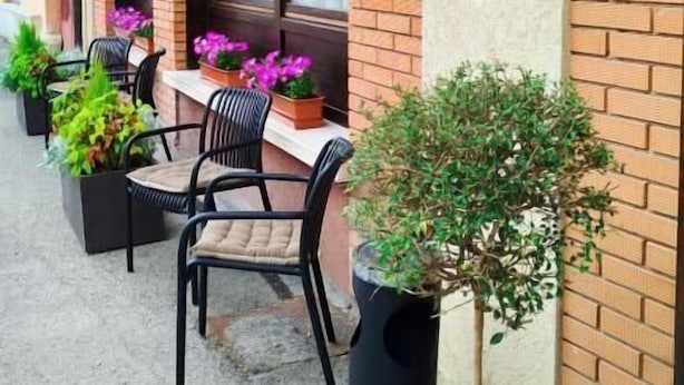 An outdoor cafe with tables and chairs, potted plants, and a brick wall. - Locanda Antica Bribano (Sedico)