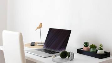A laptop on a desk with a remote control, headphones, and three potted plants.