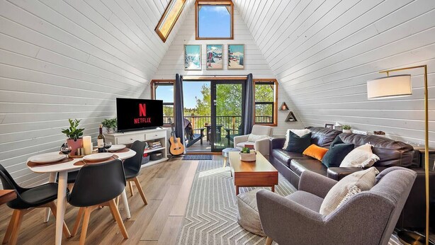 A cozy loft-style living space with a dining area, a TV, and a balcony with a view.