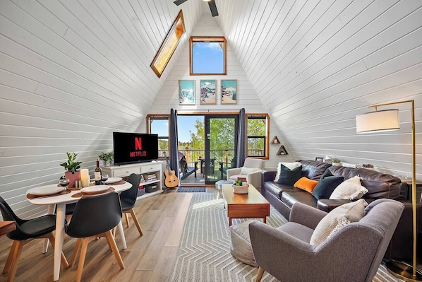 A cozy loft-style living space with a dining area, a TV, and a balcony with a view.