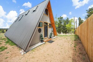 Una casa tipo cabaña con techo metálico, fachada de madera y un pequeño porche.