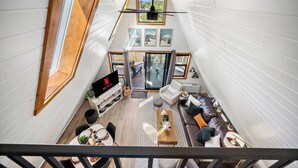A loft-style interior with a dining area, seating, a TV, and a view through a large window.