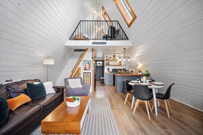 Un interior estilo loft con comedor, cocina y habitación en un entrepiso con balcón.