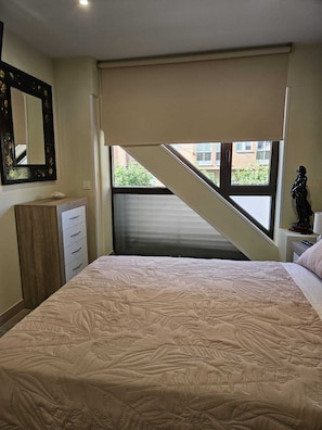 A bedroom with a bed, dresser, mirror, window, and a statue.