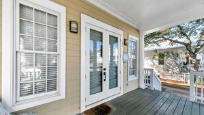 Eine Veranda mit Holzdeck, einer weißen Tür mit Fensterteil und einem kleinen Geländer.