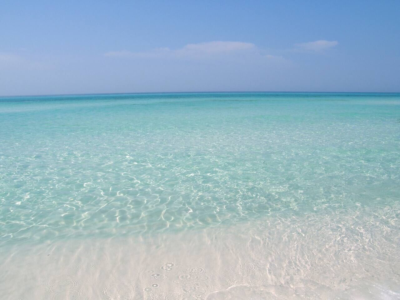 Ein Strand mit klarem türkisblauem Wasser und weißem Sand.