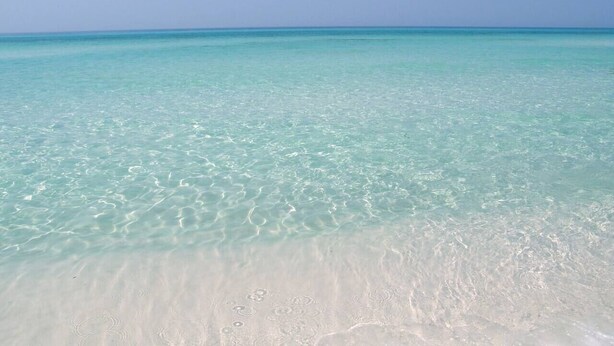 Ein Strand mit klarem türkisblauem Wasser und weißem Sand.