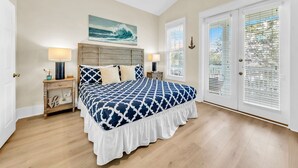 Ein Schlafzimmer mit einem großen Bett, zwei Nachttischen, einem Deckenventilator und Blick ins Freie durch ein Fenster mit Jalousien.