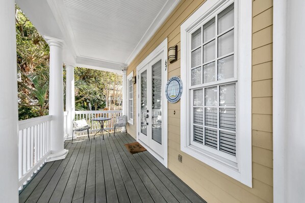 A covered porch with a white railing, a small table, and chairs. - Destin Beach Vibes, sleeps 13, 2min walk to private beach, heated community pool (Destin)