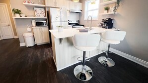 A modern kitchen with white cabinetry, a central island, two white bar stools, a microwave, and a coffee machine. - Chic Stay in Wortley – Walk to Downtown & Parks (London)