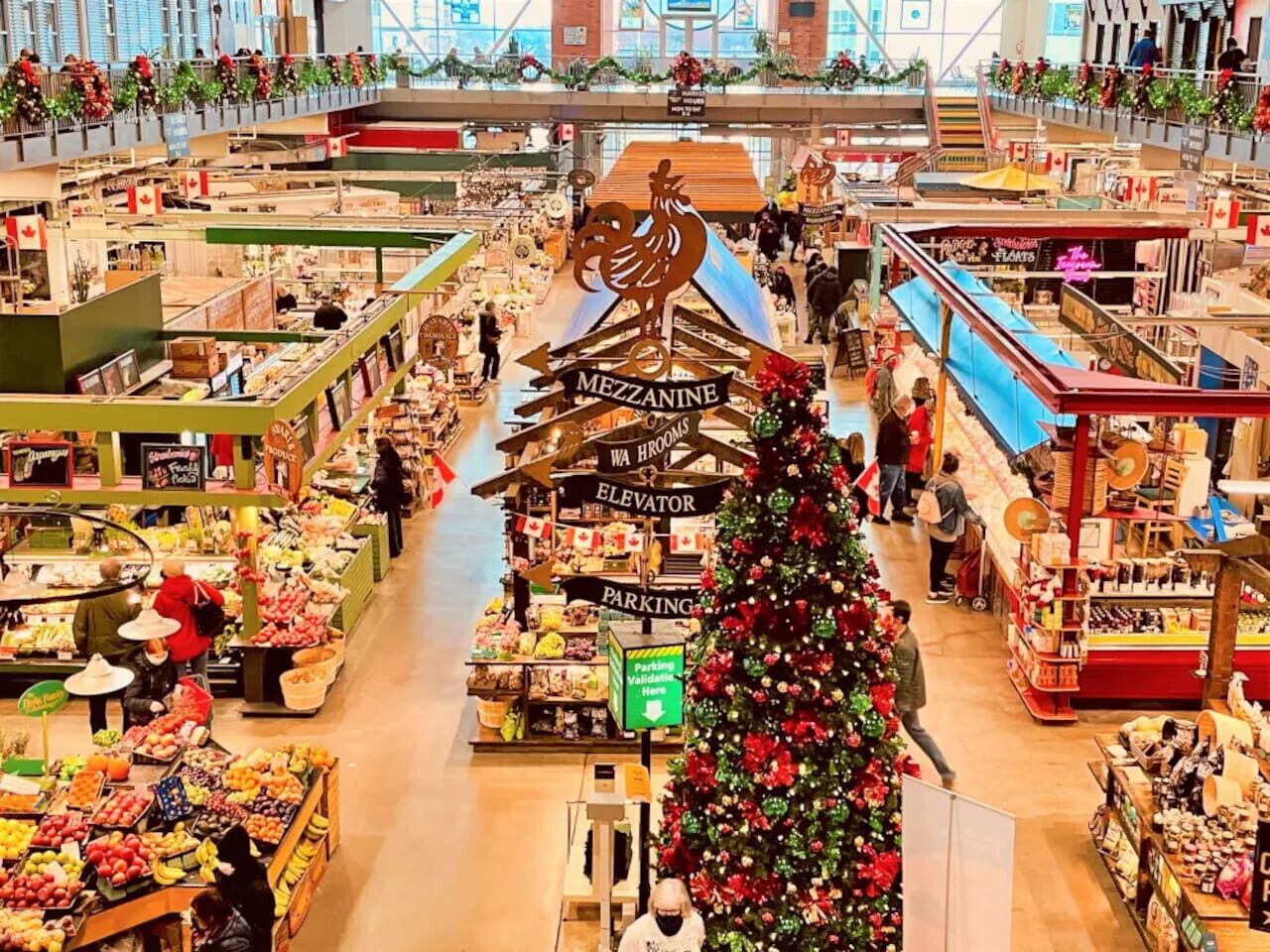 Un grand marché couvert abritant de nombreux stands de nourriture, un sapin de Noël central et des panneaux indiquant les directions et les services disponibles.