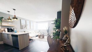 A modern kitchen with a dishwasher, a dining area with a wooden table and chairs, and a living room with a sofa and a coffee table.