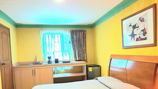 Une chambre d’hôtel avec un lit, un bureau avec un ordinateur, une fenêtre avec des rideaux et un tableau au mur.