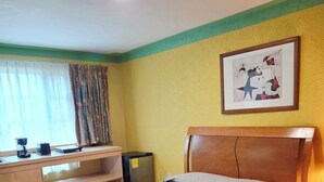 Une chambre d’hôtel avec un lit, un bureau, une chaise, une machine à café et un tableau encadré au mur.