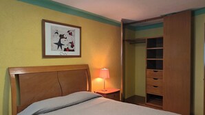 Une chambre à coucher avec un lit, une lampe de chevet, un tableau encadré au mur et une armoire en bois.
