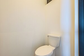 Eine weiße Toilette in einem Badezimmer mit schlichten Wänden und einer dunkelblauen Tür.