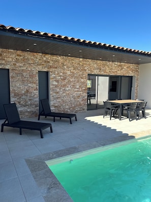A stone building with a tiled roof, a pool, lounge chairs, and a dining table with chairs. - Brand-new Villa Ô Baya, 2 minutes from shops and 5 minutes from downtown and shops. (Vallon-Pont-d'Arc)