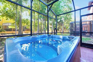 Een hottub met glazen omheining, omringd door bomen en een gebouw.