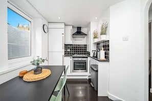 A compact kitchen with a dining area, a black stove, a microwave, and a sink. - Chic Arlington Home | Walk to Angel & King’s Cross (Greater London)
