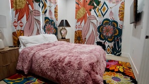 A bedroom with a bed, a nightstand, a lamp, and a TV on the wall.