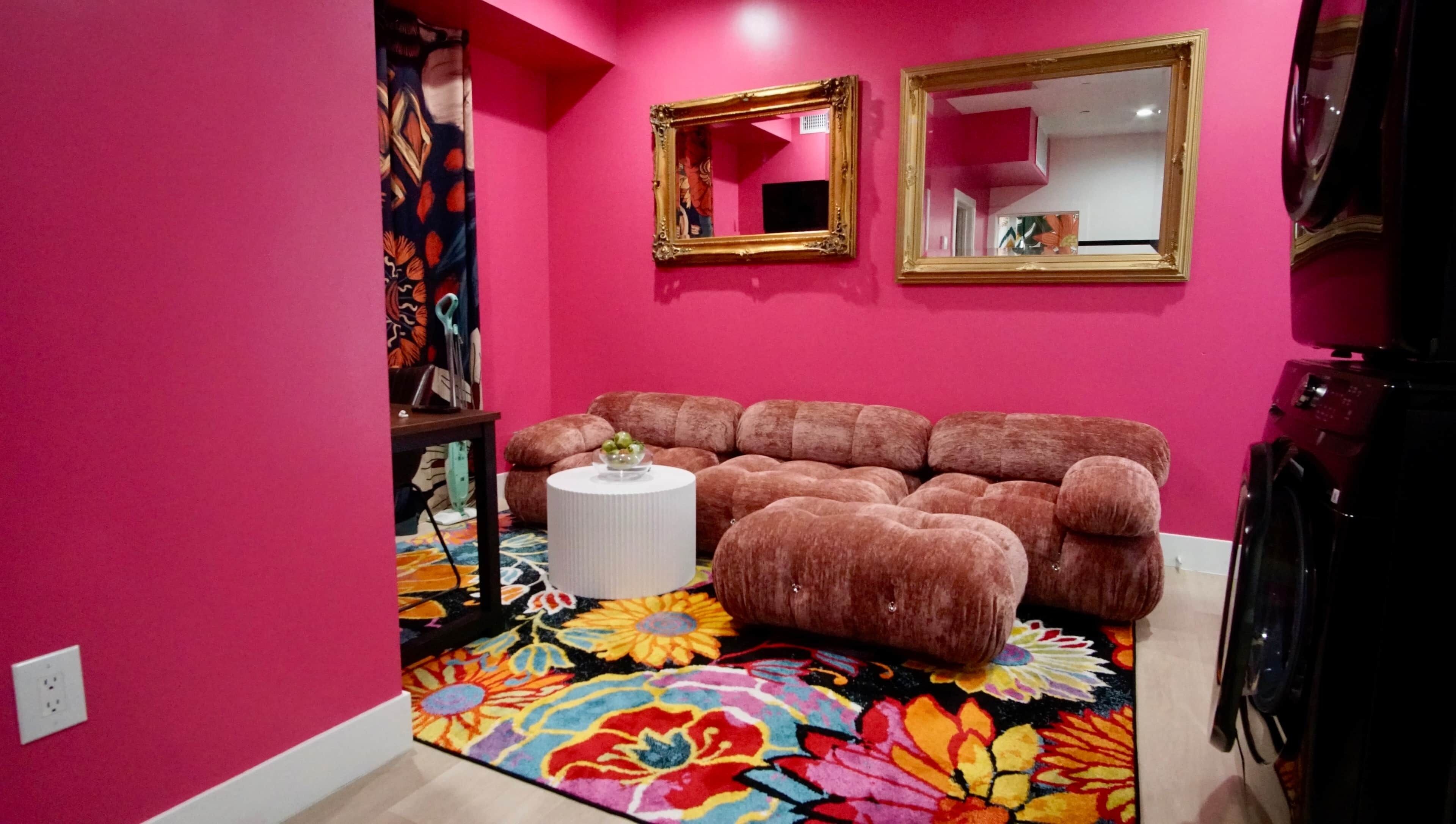 Una habitación con paredes rosadas, un sofá, un reposapiés y una pequeña mesa con un cuenco.
