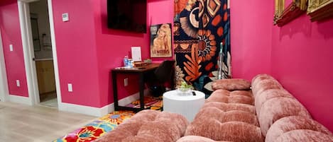 A pink-themed room with a sofa, a small table, and a tapestry.
