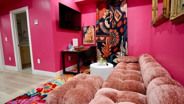 A pink-themed room with a sofa, a small table, and a tapestry.