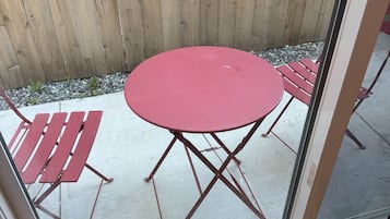 Een terras met een ronde tafel en twee stoelen, een houten hek en een glazen deur.