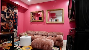 A pink-walled room with a sofa, two mirrors, and a patterned rug.