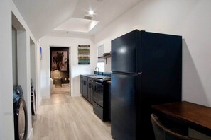 A compact kitchen with a black refrigerator, a dining table, and a washing machine. - Maison Atelier | Centrally Located | Designer 1bd (Los Angeles)