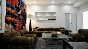 Ein modernes Wohnzimmer mit einem Ecksofa, einem Glastisch, einer Stehlampe und einem großen Spiegel an der Wand.