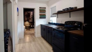 A modern kitchen with a stove, sink, and wooden shelves. - Maison Atelier | Centrally Located | Designer 1bd (Los Angeles)