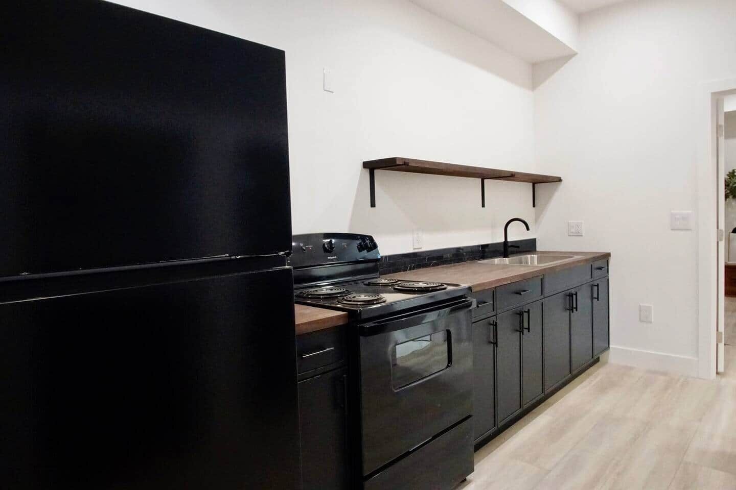 Une cuisine moderne avec un réfrigérateur noir, une cuisinière en acier inoxydable et un plan de travail en bois.