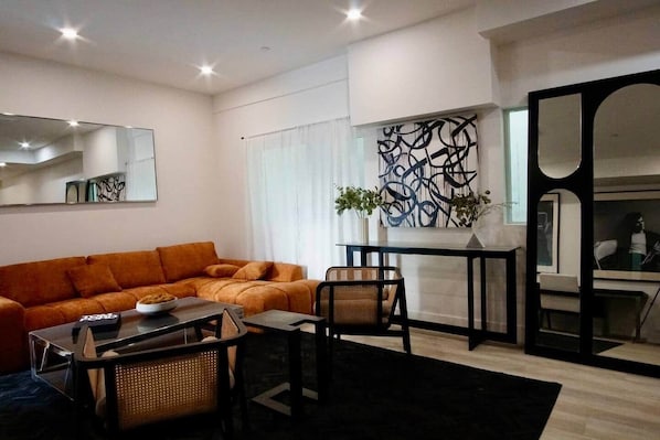 A modern living room with a sofa, a dining table, chairs, a coffee table, and a decorative wall piece. - NoHo Urban Retreat | Centrally Located (Los Angeles)