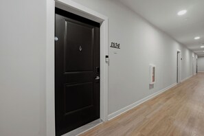 A hallway with a black door marked '1104,' white walls, and a wooden floor. - Modern Midtown ATL Escape 1BR Near The Beltline (Atlanta)