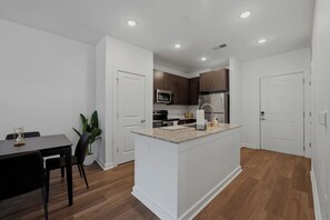 Una cocina moderna con armarios blancos, una isla central y una zona de comedor con mesa y sillas.