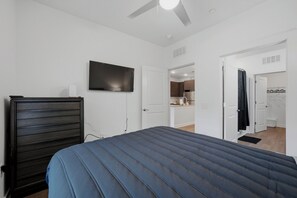 A bedroom with a bed, a TV mounted on the wall, a ceiling fan, and an open door leading to a kitchen area. - Modern Midtown ATL Escape 1BR Near The Beltline (Atlanta)