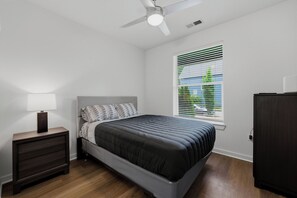Un dormitorio con cama, mesita de noche, cómoda, ventilador de techo y ventana con persianas.