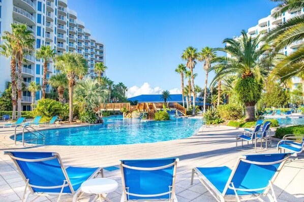 A resort pool area with multiple lounge chairs, palm trees, and a clear blue sky. - 2815 Gorgeous Gulf Views ~ Pools ~ Bar ~ Gym ~ Pickleball & More ~ Book Oct 26th (Destin)