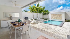 A modern outdoor dining area with a pool, lounge chairs, and a ceiling fan. - #4 Porter's Place - by Zenbreak (Holetown)