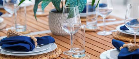 A wooden table set with plates, napkins, and glasses, with a woven placemat and a potted plant.