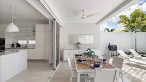 A modern kitchen with a dining area, a ceiling fan, and a patio with lounge chairs and a grill. - #4 Porter's Place - by Zenbreak (Holetown)