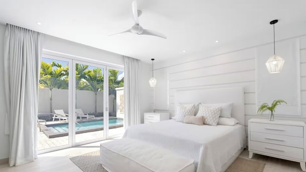 A modern bedroom with a large bed, a ceiling fan, a nightstand, and a view of a pool through glass doors. - #4 Porter's Place - by Zenbreak (Holetown)