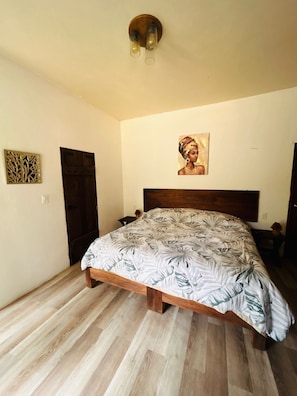 Een slaapkamer met een houten bed, een wandlamp, een deur en een ingelijst schilderij.