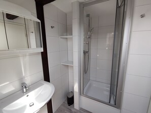A modern bathroom with a white sink, mirror, and shower enclosure.