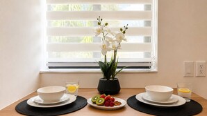 A dining table with two white bowls, a plate with kiwi and strawberries, a glass of orange juice, and a vase with white orchids. - Modern Suite King Bed Free Parking (Pembroke Pines)