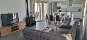A modern living room with a flat-screen TV, a fireplace, grey sofas, and a dining area with chairs and a table. - Villa Mi Atardecer (Torrevieja)