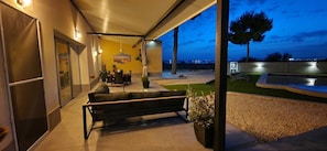 An outdoor patio with a bench, a dining table, and chairs, a yellow wall with artwork, and a view of the cityscape at dusk. - Villa Mi Atardecer (Torrevieja)