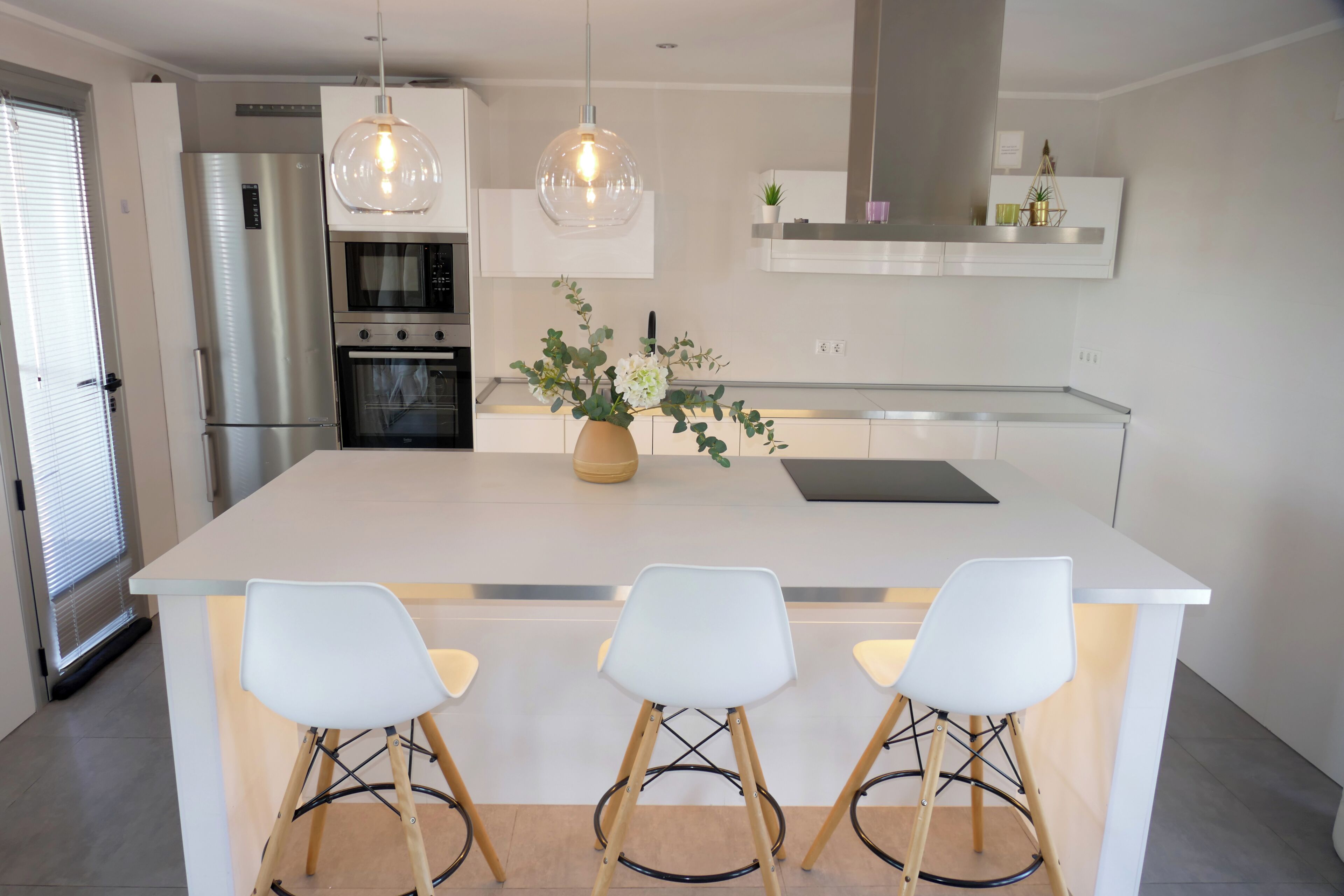 A modern kitchen with a central island, bar stools, pendant lights, and built-in appliances.